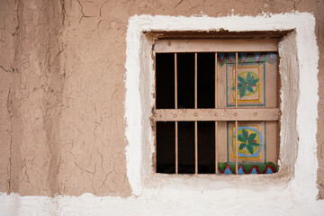 Traditional Saudi mud-house window with hand-painted wooden shutters and rustic clay walls, showcasing authentic Najdi architecture and cultural craftsmanship found in heritage villages across Saudi A