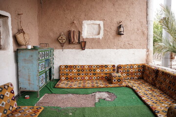 Traditional Saudi sitting area featuring patterned floor cushions, a hand-painted wooden cabinet, and rustic mud-brick walls, showcasing authentic Najdi heritage and classic Arabian interior design.