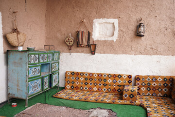 Traditional Saudi sitting area featuring patterned floor cushions, a hand-painted wooden cabinet, and rustic mud-brick walls, showcasing authentic Najdi heritage and classic Arabian interior design.