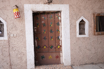 Close-up of a traditional wooden door decorated with colorful geometric and floral patterns, set beside a textured beige wall. A rustic detail reflecting cultural heritage and handcrafted design.