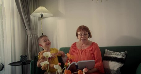 Grandma and her little grandson reading a book, child with grandma, smiling, expressing happiness, grandchild with loving grandma at home, enjoying reading fairy tales together. - Powered by Adobe