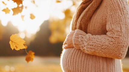 Pregnant woman embracing autumn in knit sweater amid falling leaves