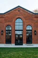 Historic brick building with large windows situated in a green landscape, showcasing detailed architecture during daylight hours
