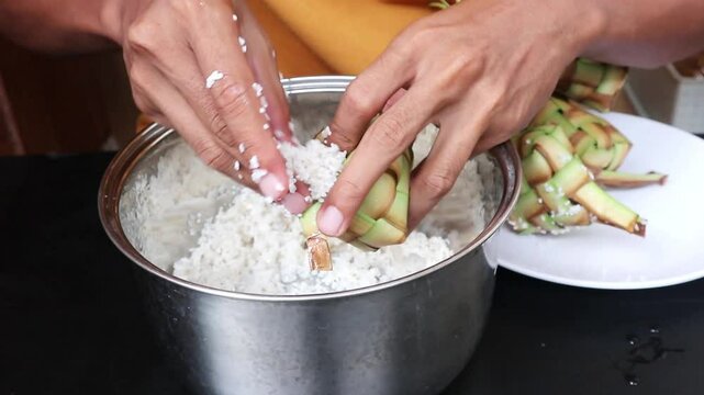 A man's hand puts rice into a ketupat. The process of making ketupat