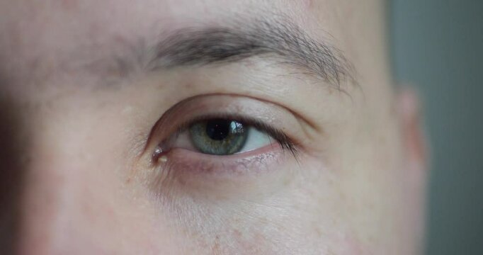 Close-up of Person's Eye With Blue-Green Iris. Blue-Green Eye of Man Looking Wincing at Camera Close Up. Motion of Human Eyes. Human Eye Iris. 