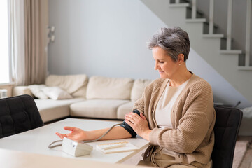 A beautiful woman in age with gray hair measures blood pressure with tonometer.