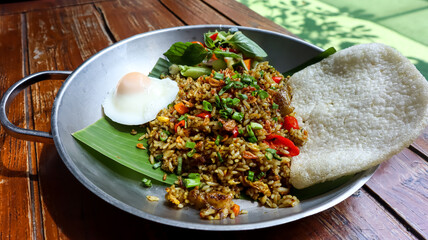 Indonesian fried rice (nasi goreng) with an egg, vegetables and crispy cracker served on a banana leaf in a silver pan