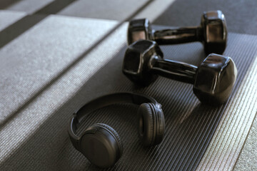 Black dumbbells for sports and acoustic headphones lie on the floor in the gym on a stylish yoga mat