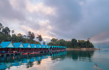 Floating village huts with incredible view of Cheow Lan Lake, surrounded by rainforest jungle and evening clouds. Stunning scenery in Surat Thani Province, Thailand.