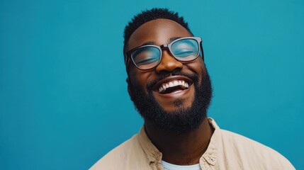 Obraz premium A joyful Black man with glasses laughs heartily against a vibrant teal backdrop. Perfect for projects needing genuine happiness and positive vibes.