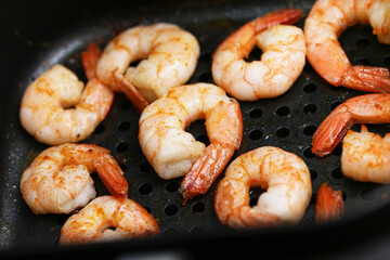 Shrimps in an air fryer background. Seafood snack cooked. Prawns with tails roasted for a healthy meal. Oil free cooking option. Quick party appetizer with crispy skin. Useful kitchen device.