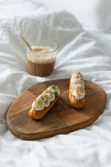 Delicious French lemon and lime merengue cream cheese eclairs on wooden tray with latte coffee for yummy breakfast in bed in the morning