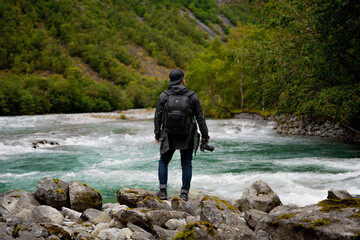 An Adventurous Photographer Stands by the Picturesque Mountain River Ready to Explore
