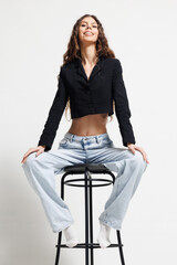 Young woman sitting on a stool wearing casual clothes and smiling confidently in a studio