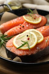 Fresh raw salmon steaks with spices in pan on wooden board, closeup