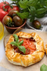 Tasty galette with tomato and basil on white tiled table, closeup