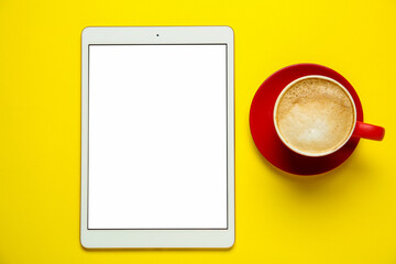Tablet with blank screen and coffee on yellow background, top view. Space for design