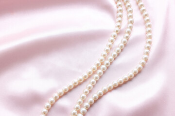 Elegant pearl necklace on pink fabric, top view. Space for text