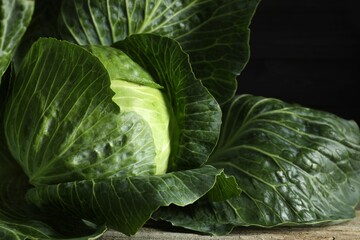 Fototapeta premium One ripe head of cabbage on wooden table against black background, closeup