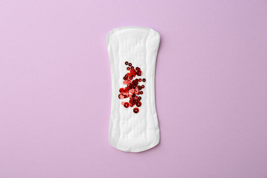 Menstrual pad with sequins on lilac background, top view