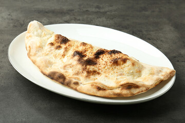 One delicious calzone on grey textured table, closeup
