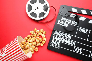 Obraz premium Movie clapper, sweet popcorn and film reel on red background, flat lay