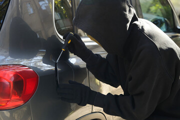 Thief with screwdriver opening fuel cap. Car hijacking