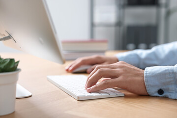 Fototapeta premium Man working on computer at wooden desk in office, closeup