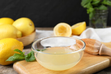 Fresh lemon juice in bowl, squeezer and fruits on wooden table, closeup