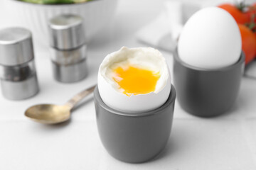 Soft boiled eggs in cups served on white table, closeup