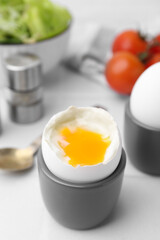 Soft boiled eggs in cups served on white table, closeup