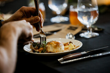 Hands cutting into a plated dish of food at a restaurant dinner event.