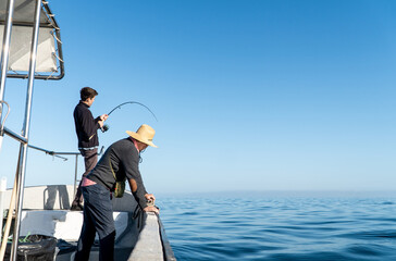 Teenager Fishing from a Boat While His Father Watches the Fish in the Water