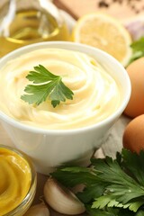 Delicious mayonnaise sauce in bowl and ingredients on table, closeup