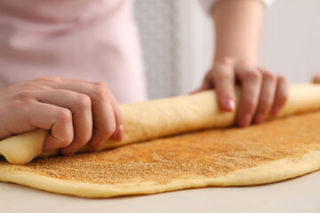 Making cinnamon rolls. Woman shaping dough at white table, closeup