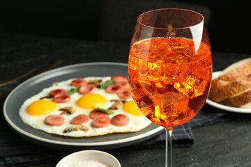 Tasty brunch. Aperol cocktail, delicious fried eggs with sausage served on black table, closeup