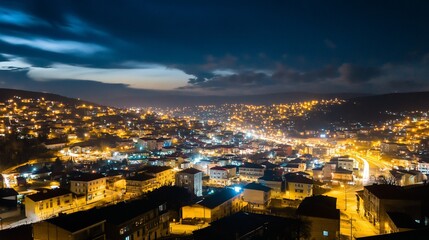 Naklejka premium Cityscape at night with illuminated buildings and a dark cloudy sky above