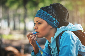 Woman, trail runner and drinking water in woods with straw, backpack or break for hydration in...