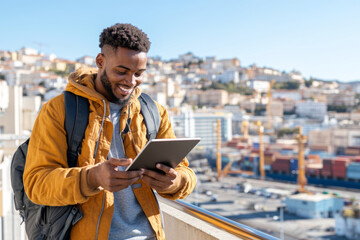 young man smiles while using tablet outdoors, with cityscape in background. scene conveys sense of joy and engagement in technology