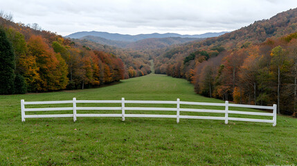 Autumnal valley view from grassy hilltop, white fence