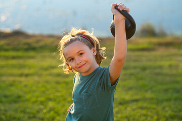 Kid boy working out with dumbbells. Sport and kids training. Child lifting the kettlebell in backyard outside.