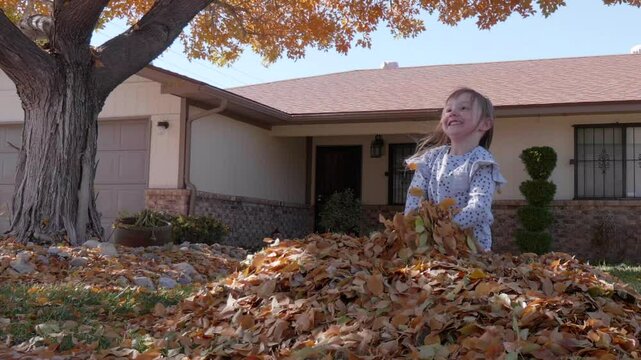 Happy Little Girl in a Leaf Pile Throwing Leaves
