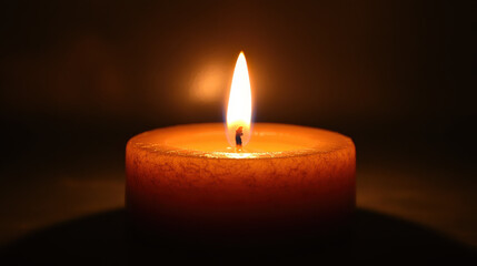 A single candle burning brightly in the darkness, its flame gently flickering. The background is a simple solid color, drawing full attention to the warm glow and wax details. The image conveys themes