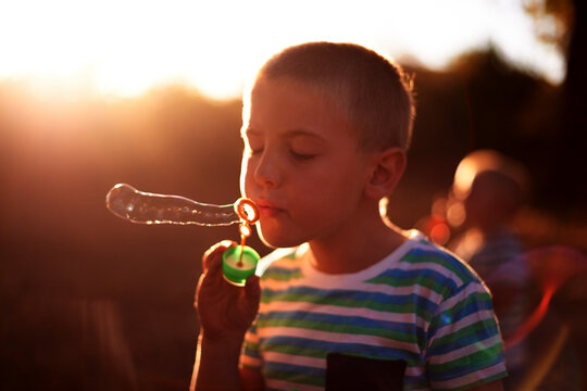 Bubbles, blowing and child in park with fun, sunset adventure and outdoor development for kids in nature. Relax, weekend and boy in garden playground with soap wand, childhood games and play activity