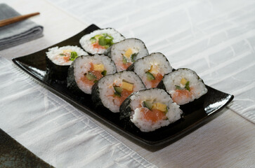 Homemade salmon salad sushi on black plate with white placemat on table. Japanese healthy food. Selective focus.