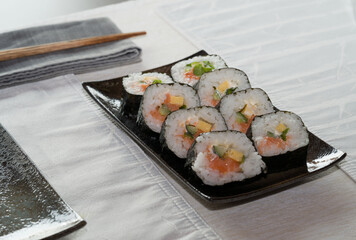 Homemade salmon salad sushi on black plate with white placemat on table. Japanese healthy food. Selective focus.