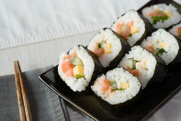 Homemade salmon salad sushi on black plate with white placemat on table. Japanese healthy food. Selective focus.