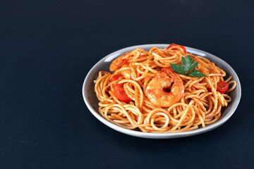Italian pasta with shrimps, parsley and tomato sauce on black background. Copy space. 