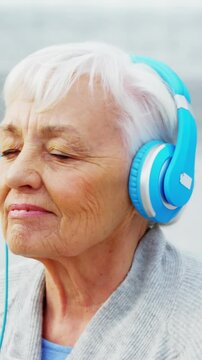 Senior woman listening music on headphone on beach