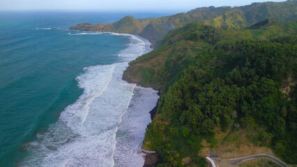 Bird eye view of the coastline with hills and trees, cliffs, coral reefs and waves from the sea at...
